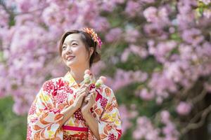 Japanese woman in traditional kimono dress holding sweet hanami dango dessert while walking in the park at cherry blossom tree during spring sakura festival concept photo