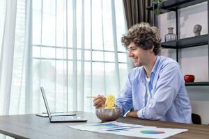 Caucasian man is working at his home office while eating instant noodle and analyzing the statistic chart for freelance and entrepreneur business concept photo
