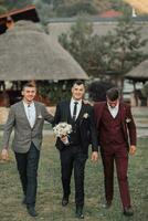 Photo of three men in classic suits. A man holds a bouquet while standing among his friends. Business style. Stylish men