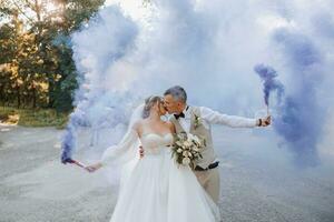 en su manos, el recién casados sostener multicolor fumar bombas de azul color. novio y novia beso. Boda divertida. foto