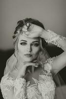 A blonde bride in a long, lacy petticoat is standing in her room, posing by the mirror, putting on her earrings. Beautiful hair and makeup, open bust. Wedding portrait. Reflection in the mirror photo