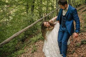 A happy wedding couple is running along a forest path. Groom and bride. Wedding photo session in nature. Photo session in the forest of the bride and groom.