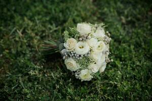 un ramo de flores de blanco rosas y verdor, atado con un cinta, mentiras en verde césped. un increíble Boda ramo. blanco rosas. belleza es en el detalles foto