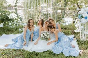 The bridesmaids are in blue dresses, the bride is holding a beautiful bouquet. Sitting enjoying the celebration. Beautiful luxury wedding blog concept. Spring wedding. photo