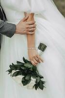 Boda foto detalles. foto de un ramo de flores de rosas y verdor, cuales es hermosamente retenida por el novia, el del novio mano en el de la novia mano. Boda anillo. plata joyería en manos