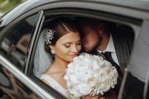 A modern bride and groom in a lace dress in a car window. Beautiful and smiling newlyweds. Happy holiday. photo