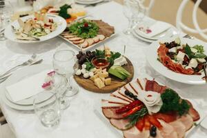 buffet mesa a un boda. queso lámina. surtido de canapés. banquete servicio. alimento, meriendas con queso, jamón, jamón y fruta. César ensalada. vaso lentes. plata mesa conjuntos foto