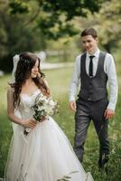 Happy stylish groom walking to the bride. The bride is in the foreground. Groom in a vest. Portrait of the groom. Spring wedding photo