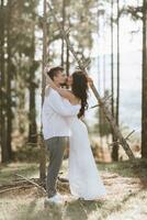 elegante novio en blanco camisa y linda morena novia en blanco vestir en bosque cerca Boda de madera arco. Boda retrato de recién casados. foto