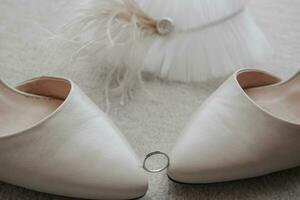 The wedding ring is held by the tips of the shoes, behind the garter is decorated with feathers, on a gray background photo