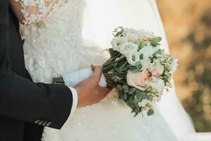 Cropped wedding photo details. The groom in a black suit and the bride in a chic white dress are holding a wedding bouquet. Beautiful hands. Portrait. Bright summer wedding