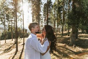 Stylish model couple in white clothes kissing at sunset in the forest. A girl hugs her husband, hair blowing in the wind. Wide angle photo