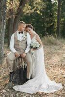 Boda foto en naturaleza. el novio es sentado en un de madera pararse, el novia es participación un ramo, en pie siguiente a a él, propensión en su hombro. retrato de el novia y novio