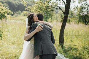 The morning of the bride and groom. The first meeting of the newlyweds and the first happy hugs. The bride smiles and tenderly hugs the groom. Spring wedding. Wedding ceremony in the forest. Emotions. photo