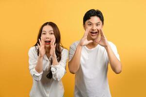 Cute young Asian couple shouting with hands isolated on yellow studio background. photo
