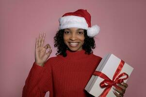 Christmas sale and celebration concept. Smiling young woman showing ok sign and holding christmas gift box photo