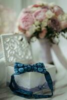 The groom's blue butterfly is standing on a wooden box with wedding rings on the background of a wedding bouquet. Wedding details. photo