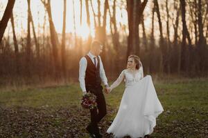 Wedding photo. The bride and groom are walking in the forest. The groom holds the hand of his beloved. Long wedding dress. A couple in love among tall trees. Autumn sunlight. photo