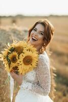 Wedding portrait. A red-haired bride in a white dress stands near a bale of hay with a bouquet of sunflowers and looking into the lens, smiling. Beautiful curls. Sincere smile. Elegant dress photo