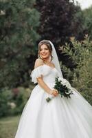 Wedding photo. The bride in a voluminous white dress and a long veil, smiling, twirling with a bouquet of white roses, holding her dress. Portrait of the bride. Beautiful makeup and hair. photo