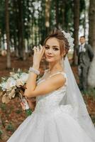 A beautiful young woman in a wedding dress between tall trees in the forest with a royal hairstyle and a chic tiara with a bouquet of flowers in her hands, a wedding in golden color photo