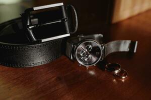 men's details, business, the watch stands stylishly on the table, next to it are wedding rings and a men's leather belt photo