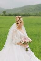 Portrait of the bride. The bride is standing in a white dress and veil with a bouquet in a green field. A wonderful dress. Pretty Woman. Wedding photo