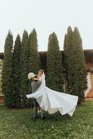 Handsome groom carrying a beautiful laughing bride in his arms in a spring park. The groom is circling with the bride in his arms photo