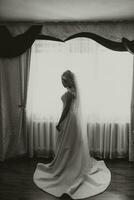 Portrait. A blonde bride in a wedding dress with a long train and a chic veil is standing and posing. Gorgeous make-up and hair. Voluminous veil. Wedding photo. Beautiful bride. black and white photo