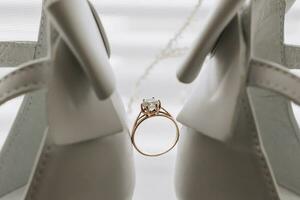 The bride's wedding ring stands between elegant white shoes on a light background. Bride's shoes and wedding ring. Wedding photography photo