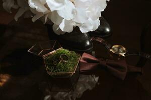 Morning of the groom and details, details of the groom on a dark background. men's watch, wedding rings in a glass box and wooden moss, a men's butterfly and a bouquet of white flowers photo