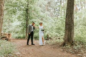 spring wedding photo of the bride and groom. Kisses the hand. forest road between tall trees. Happy wedding couple