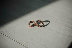 Wedding golden rings in beautiful daylight, on a white wooden background. Shadow. Wedding accessories. photo