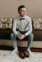 portrait. A man in a white shirt and gray pants is sitting on a sofa next to elegant red men's shoes. A stylish watch. Men's style. Fashion. Business photo