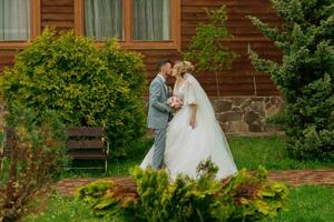 Wedding in nature. Photo of bride and groom on a walk against the background of trees, bride and groom kissing against the background of trees and a wooden hut. Stylish groom. Beautiful bride.