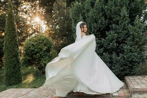 Wedding photo. The bride in a voluminous white dress and a long veil, smiling, twirling with a bouquet of white roses, holding her dress. Portrait of the bride. Beautiful makeup and hair. photo