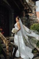 Romantic full-length portrait of a brown-haired woman in a white dress with a bouquet standing near the wooden gate of the church entrance photo