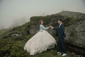 Happy wedding couple in the mountains near a big stone holding hands. Wedding photo session in nature. Photo session in the forest of the bride and groom.