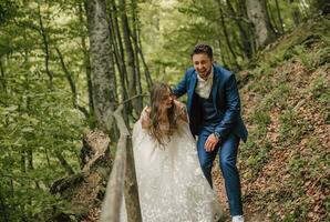 A happy wedding couple is running along a forest path. The bride smiles sincerely. Wedding photo session in nature. Photo session in the forest of the bride and groom.