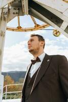 A man among the mountains, near the construction of a mountain lift, a groom and a brown suit photo