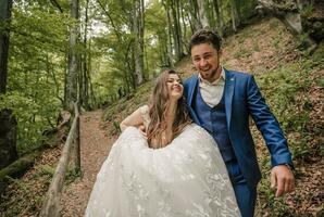 A happy wedding couple is running along a forest path. The bride smiles sincerely. Wedding photo session in nature. Photo session in the forest of the bride and groom.