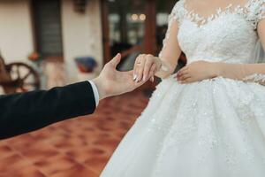 Wedding portrait in nature. Cropped photo of beautiful hands. Bride and groom brunette in white long dress holding hands. French manicure. Stylish groom.