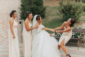 Wedding photo in nature. A brunette bride in a white long dress and her friend in a nude dress are fooling around together and smiling sincerely. Young women. emotions