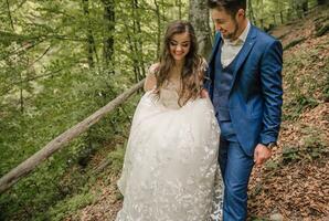 A happy wedding couple is running along a forest path. The bride smiles sincerely. Wedding photo session in nature. Photo session in the forest of the bride and groom.