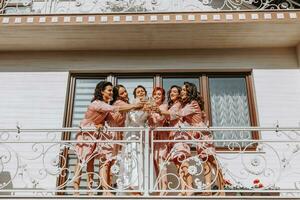 Young bridesmaids are having fun and smiling in pink silk robes drinking champagne at the bride's gazebo. Beautiful women celebrate a bachelorette party, in a gazebo and with champagne. photo