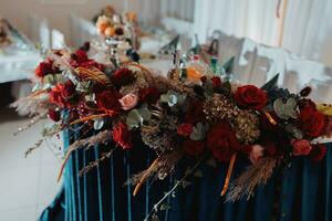 el Boda mesa de el novia y acicalar, decorado con rojo flores, azul terciopelo, es hecho en rojo y azul. flores en soportes Boda detalles. ligero foto