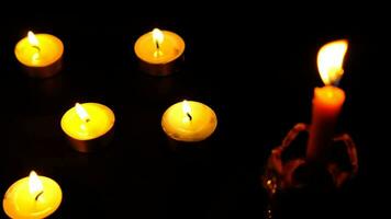 Many candles lit against a black background.Burning candles on dark tableMemory video