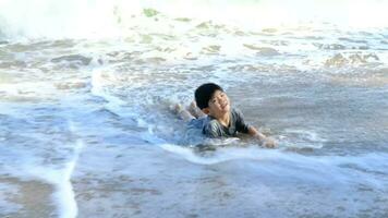 liten asiatisk pojke spelar i de sand på de hav strand video