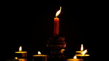 Many candles lit against a black background.Burning candles on dark tableMemory video