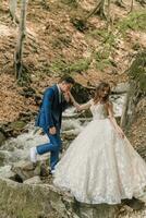 The bride is holding her dress, he kisses her hand. Groom and bride. Wedding photo session in nature. Photo session in the forest of the bride and groom.